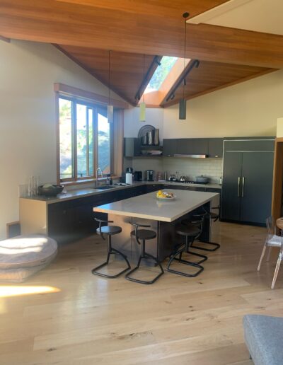 Modern kitchen interior with high ceilings, a central island with bar stools, and natural lighting.