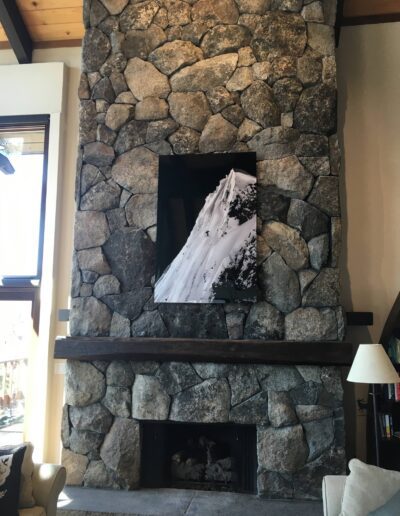 A large stone fireplace with a mounted flat-screen television displaying a snow-covered mountain slope.