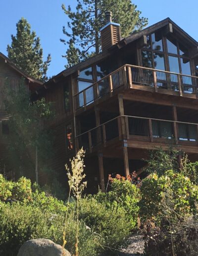 A large wooden cabin with multiple decks surrounded by trees on a sunny day.