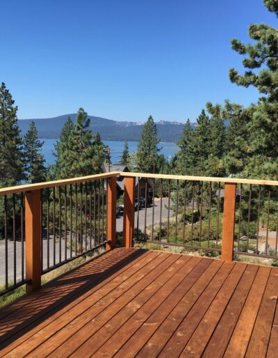 Wooden deck overlooking a lake with surrounding pine trees under a clear blue sky.